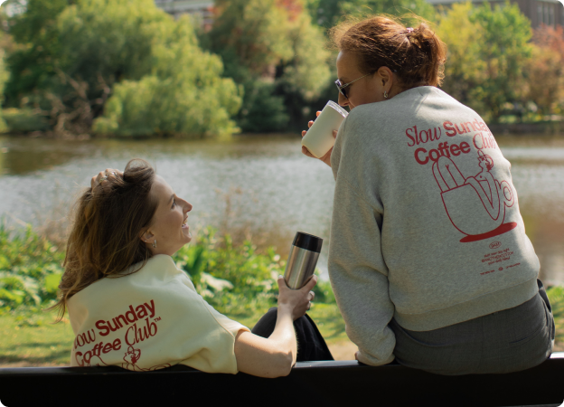 Two people sitting by a lake, wearing 'Sunday Coffee Club' shirts.