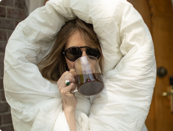 Person wrapped in a large white blanket, holding a glass mug of drip coffee.