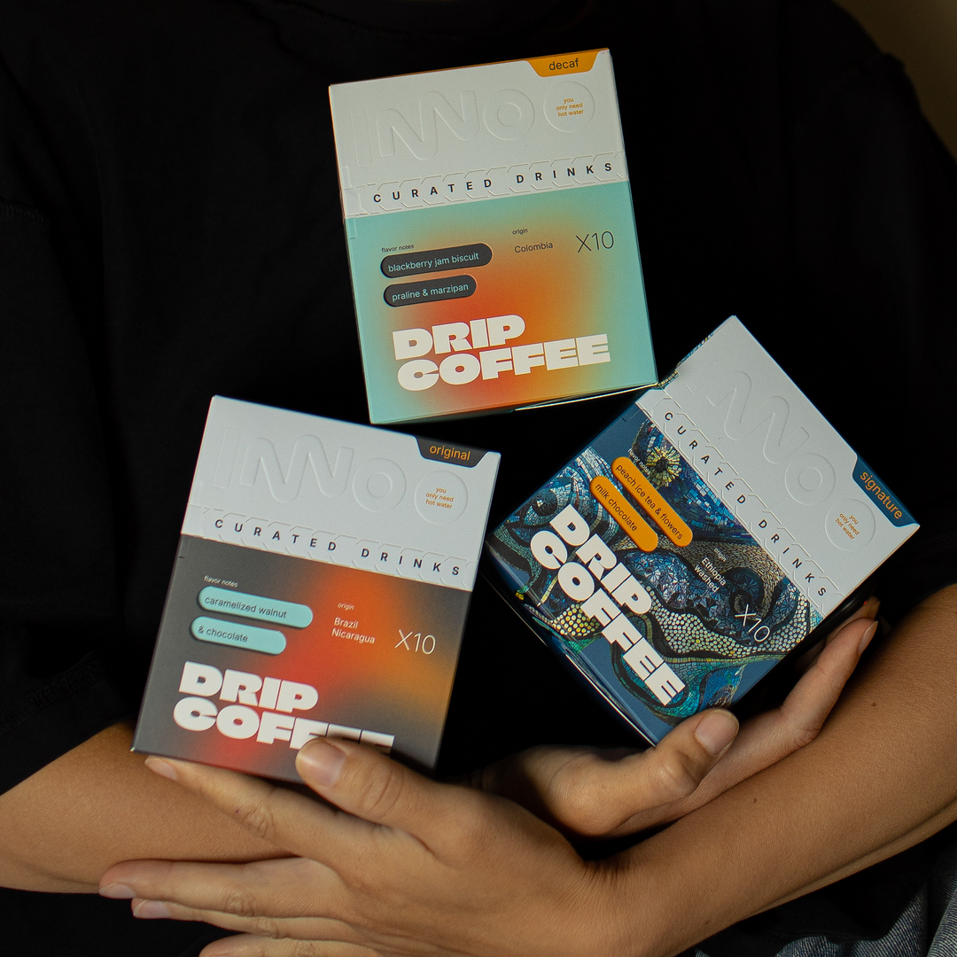 Three boxes of INNO Specialty Drip Coffee held by a person against a dark background.
